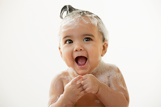 Criança pequena com cabelo ensaboado, se divertindo ao tomar banho com sabonete de glicerina para bebê. 