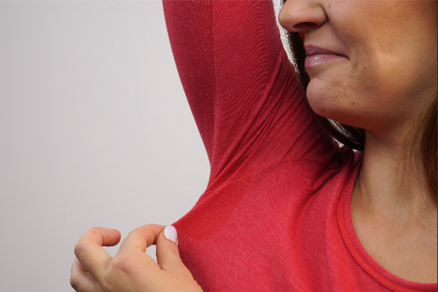 Pessoa cheirando a blusa na axila, incomodada com o suor na adolescência, comum devido às mudanças hormonais dessa fase.